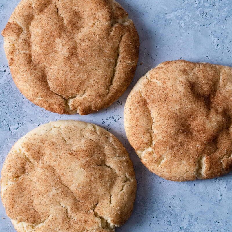 Dairy-free Snickerdoodle Cookies from Grandma's Cookies, showing three classic cookies with signature crackly tops and cinnamon-sugar coating. Each displays our characteristic hand-scooped texture and golden-brown color.