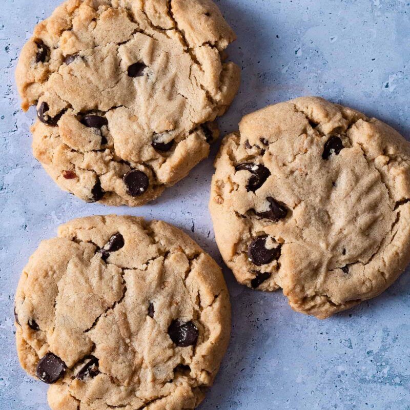 Peanut Butter Chocolate Chip Cookies from Grandma's Cookies, featuring three cookies with rich chocolate chunks scattered throughout golden peanut butter dough. Each shows our signature hand-scooped texture with classic crinkled top.