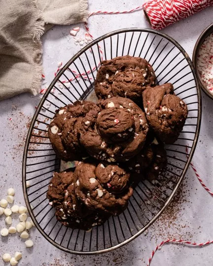 Double chocolate cookies on black striped platter with festive red and white twine. Rich dark cookies topped with white chocolate chips and cocoa powder dusting.