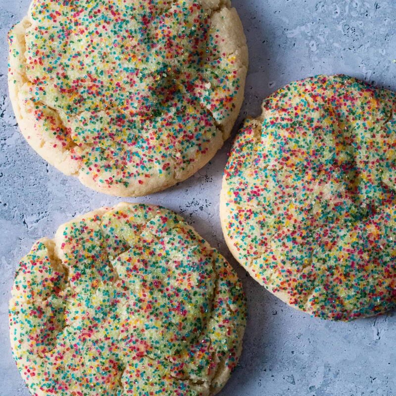 Dairy-free Sugar Sprinkle Cookies from Grandma's Cookies, showing three freshly baked cookies topped with festive red and green sprinkles. Each cookie features our signature hand-scooped texture and generous sprinkle coating.