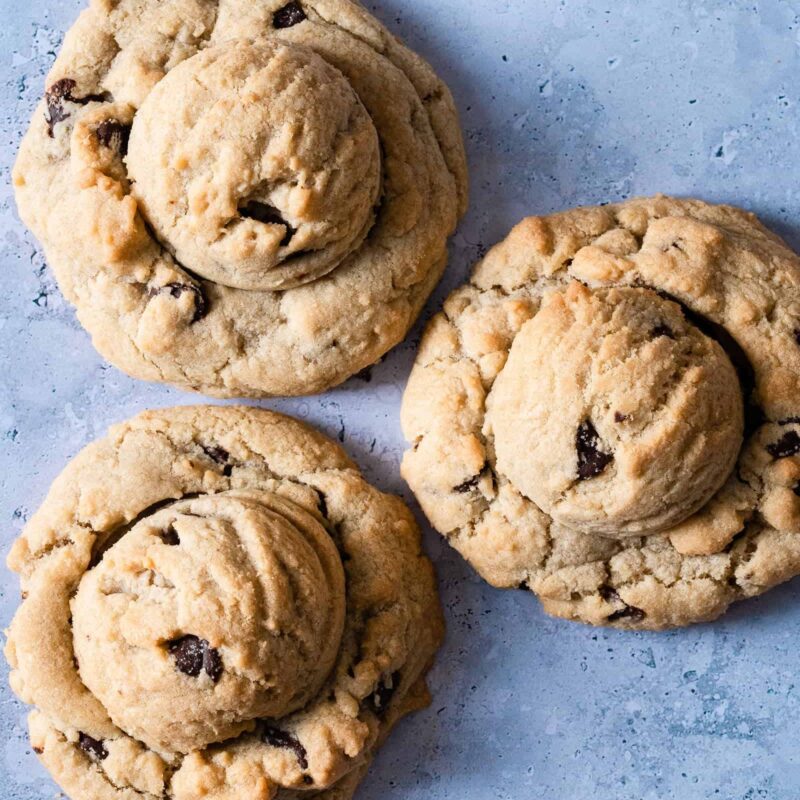 Soft-Baked Chocolate Chip Cookies from Grandma's Cookies, featuring three generously-sized cookies with our signature double-decker stacked appearance. Each cookie showcases our classic hand-scooped texture with a buttery golden dough studded with dark chocolate chips. The cookies display characteristic crackly tops and perfectly crisp edges while maintaining their thick, pillowy centers.